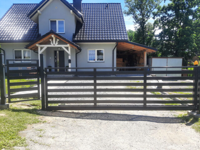 Nowoczesna brama przesuwna z poziomymi profilami przed jednorodzinnym domem z piętrem